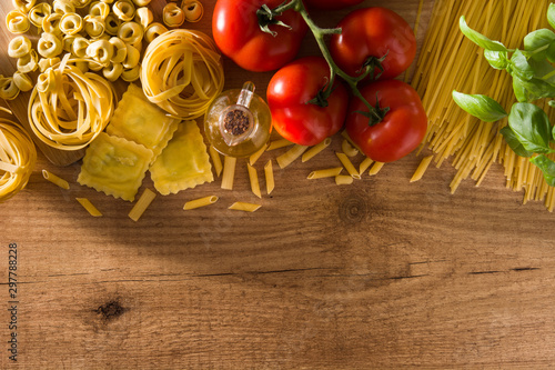 Italian pasta and ingredients. Ravioli, penne pasta, spaghetti, tortellini, tomatoes and basil on wooden table