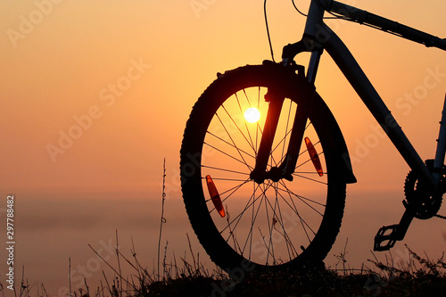 Silhouette of a bicycle against the orange sky at sunrise