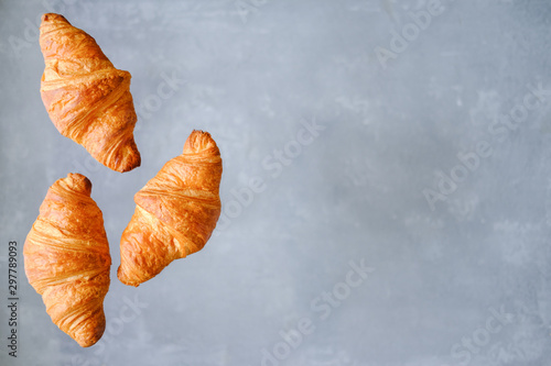 Three freshly baked croissants fly on grey background. Place for text. Creative bakery concept.