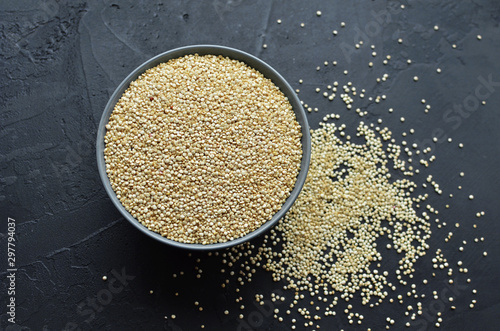 Dry organic quinoa seeds in gray ceramic bowl on dark concrete background