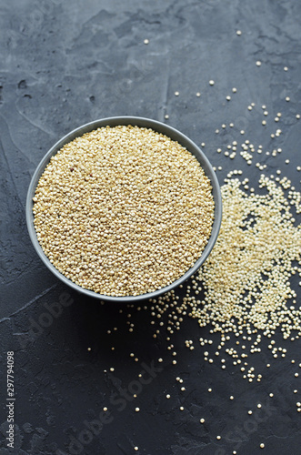 Dry organic quinoa seeds in gray round ceramic bowl on dark concrete background
