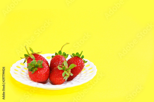 natural red strawberries with green leaves in a white decorative plate on a yellow background