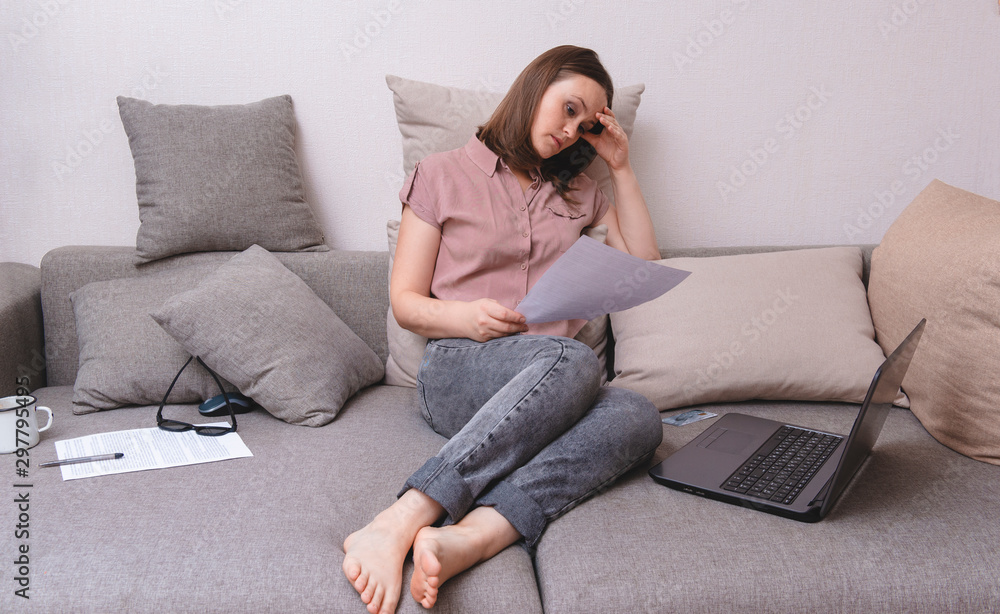 white woman sitting on couch and looking at document with tense tired expression, laptop , white woman sitting on couch and looking at document with tense tired expression, laptop ,