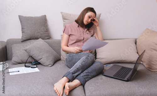 white woman sitting on couch and looking at document with tense tired expression, laptop ,