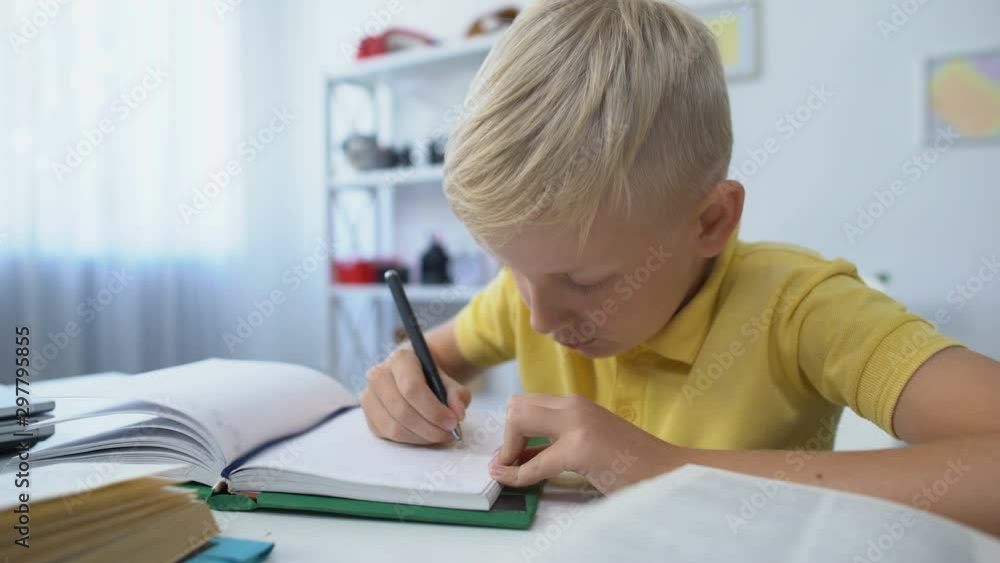 Smart male child doing homework, writing in notebook, education and knowledge Smart male child doing homework, writing in notebook, education and knowledge