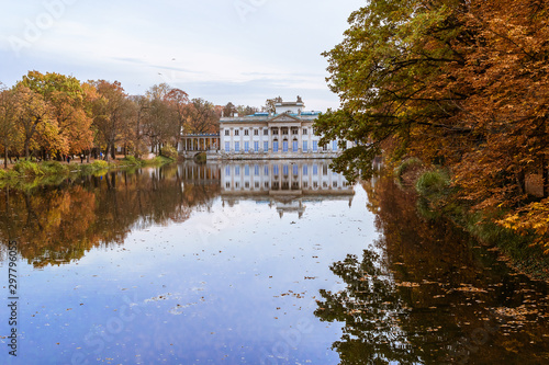 Autumnal landscape with the Baroque building of the Palace on the Isle and water under the blue sky in Warsaw Royal Baths Park, Poland