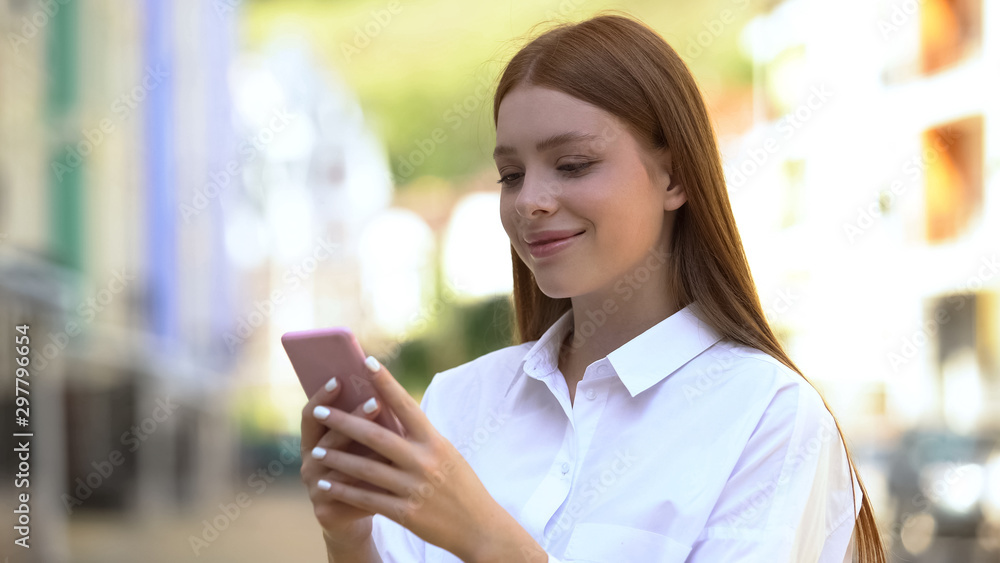 Cheerful caucasian girl messaging on smartphone outdoor and smiling, application