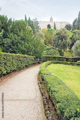 Lane going along green lawn in an old Italian park with remote building on a hill