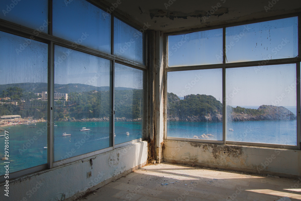Large window of an abandoned hotel with the view to an ocean bay