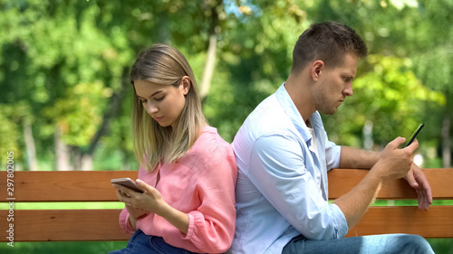 Girlfriend boyfriend sitting back scrolling phones ignoring each other, conflict © motortion
