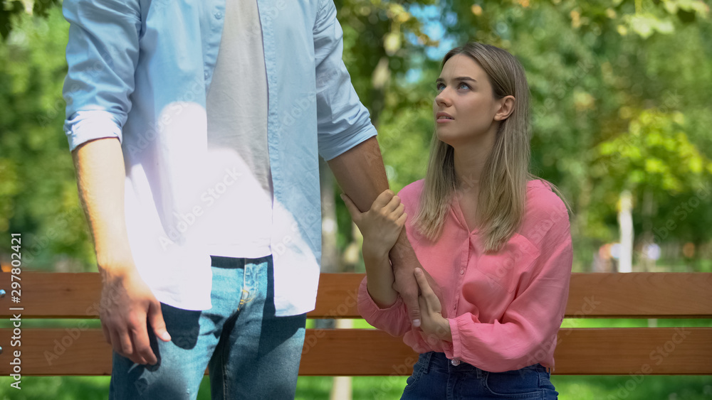 Man leaving upset girlfriend alone on bench in park walking away, break-up