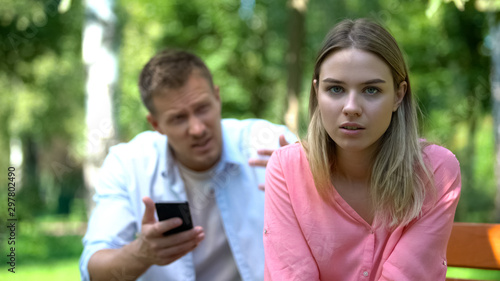 Young woman looking camera feeling tired of annoying boyfriend checking phone