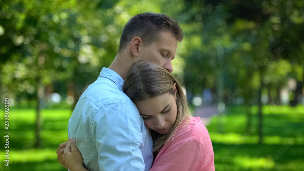 Man hugging and comforting upset girlfriend in park, togetherness and support Man hugging and comforting upset girlfriend in park, togetherness and support