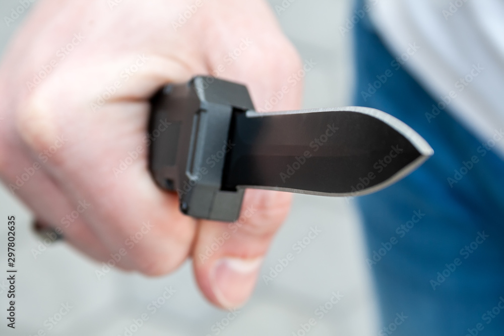 Closeup view of a man's hand with a black pocket folding knife blade facing forward. Selective focus