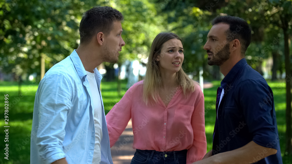 Young female trying to calm down angry men arguing outdoors, relations jealousy