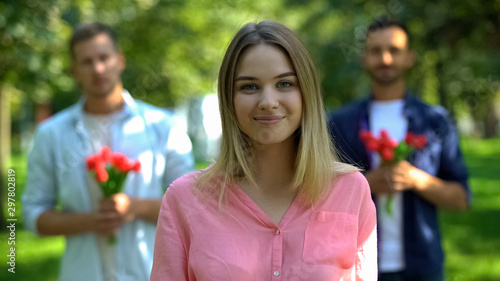 Glad young woman with two admirers holding flowers on background, love choice