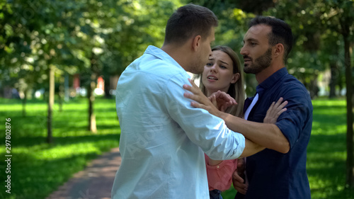 Frightened woman standing between fighting men, rivalry for woman attention