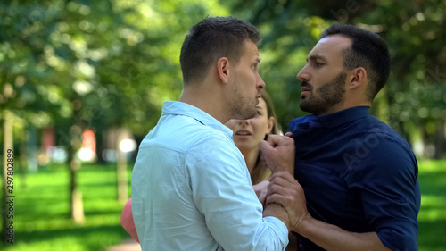 Angry boyfriend pushing man fighting outdoors, girlfriend trying to calm down