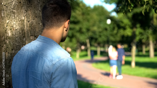 Man secretly spying loving couple walking on date outdoors, jealous ex-boyfriend photo