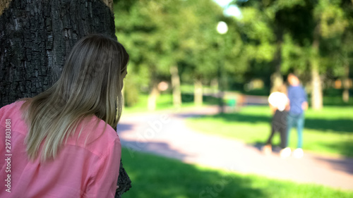 Obraz na plátně Woman looking at loving couple walking outdoor date hiding behind tree in park