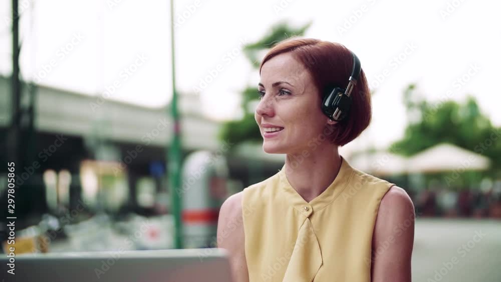 Young businesswoman with headphones and laptop sitting in cafe outdoors in city. Young businesswoman with headphones and laptop sitting in cafe outdoors in city.