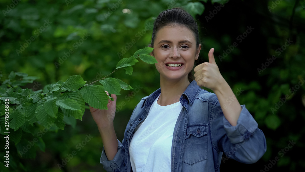 Attractive young female holding forest tree leaves showing thumbs up eco project Attractive young female holding forest tree leaves showing thumbs up eco project
