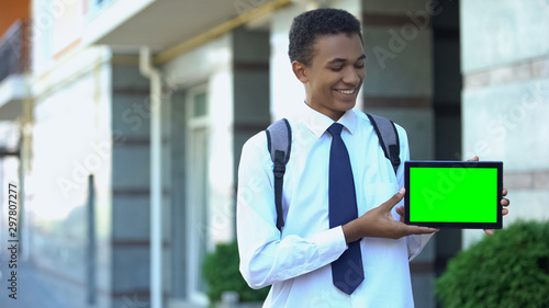 Smiling Afro-American teen student showing presentation on green screen tab