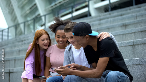 Happy university students watching online video by smartphone having fun, gadget