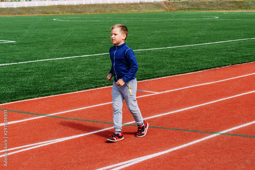 eight-year-old Caucasian boy in sports uniform runs on the red treadmill at the stadium eight-year-old Caucasian boy in sports uniform runs on the red treadmill at the stadium