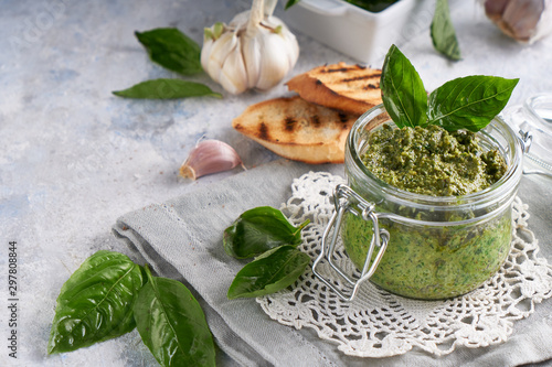 traditional italian basil pesto sauce in a glass jar wiht toasts on a light stone table Copysapce