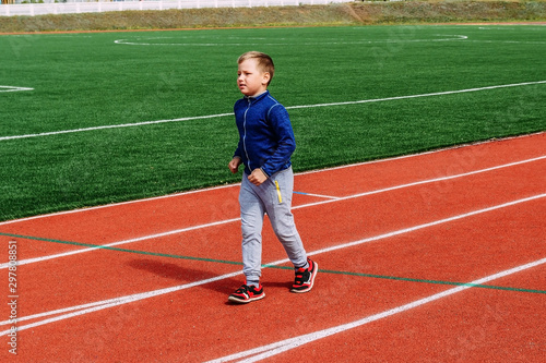 eight-year-old Caucasian boy in sports uniform runs on the red treadmill at the stadium