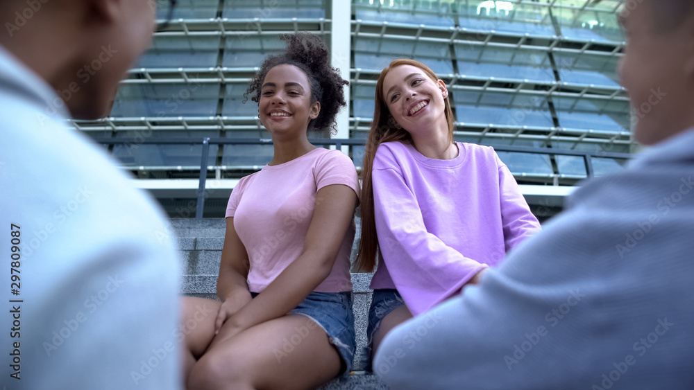 Young female students looking at male classmates, friends spending time outdoors
