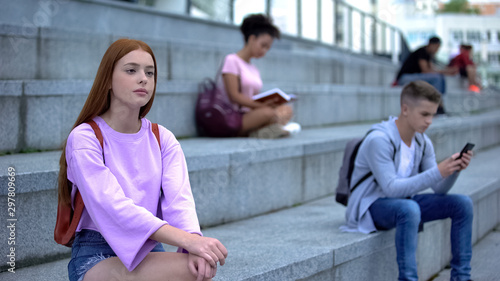 Upset female student sitting alone campus stairs, unsociable teenager problems