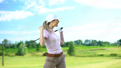 Fotografi Joyful female golf player with club gesturing yes sign rejoicing successful shot