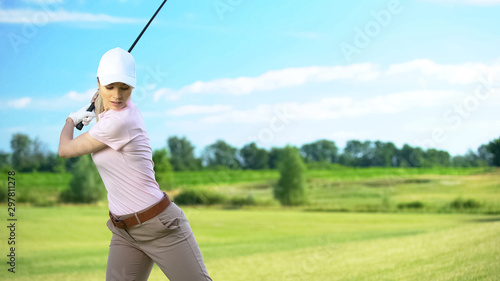 Slim woman with golf club performing swing hitting ball, luxury hobby, sport