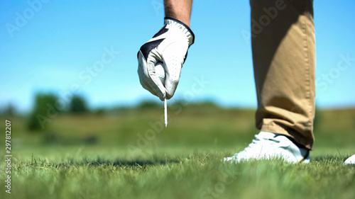 Golf player hand teeing off golf ball before swing, professional sport, hobby