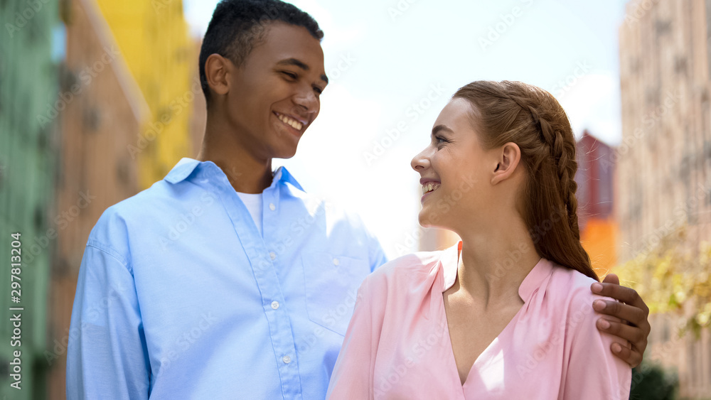Positive mixed race couple looking at each other and laughing, togetherness Positive mixed race couple looking at each other and laughing, togetherness