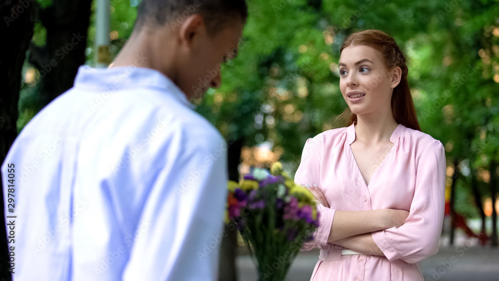 Shy mixed-race teen boy presenting bunch of flowers to girl, inviting for date Shy mixed-race teen boy presenting bunch of flowers to girl, inviting for date
