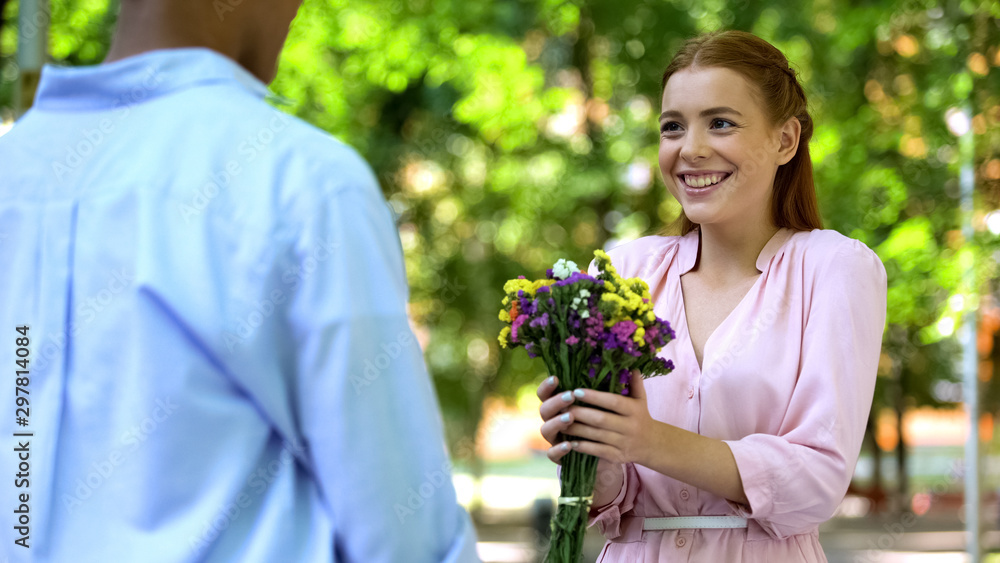 Mixed-race teen boy presenting flowers to surprised girlfriend, date in park