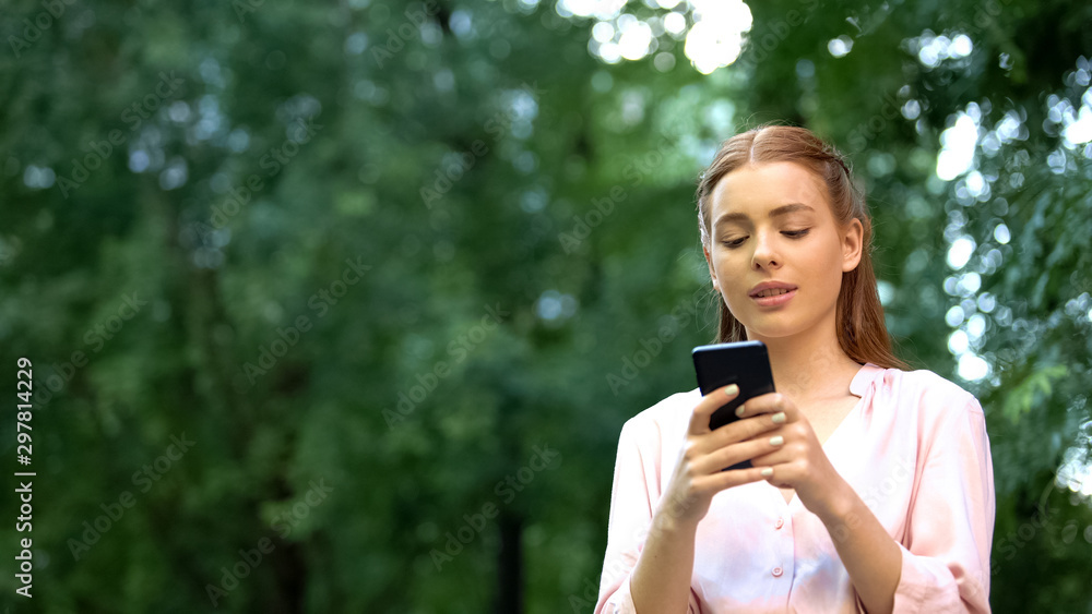 Beautiful young girl chatting on smartphone spending time outdoor, addiction