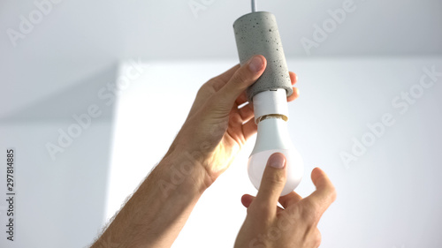 Photography Male hands twisting electrical saving lightbulb, energy efficiency, closeup