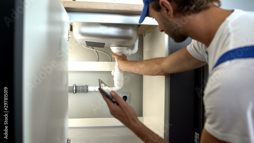 Cuadro en lienzo Professional plumber checking water pipes in kitchen, typing report in tablet