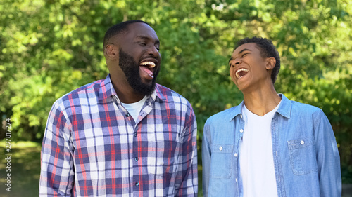 Positive son and father laughing outdoors joking having fun together, relations
