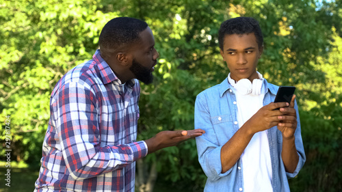 Fotografie Father scolding male teen son playing smartphone game ignoring parent upbringing