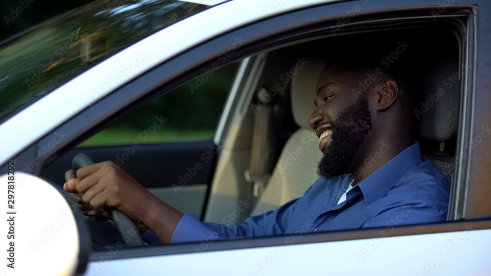 Cheerful adult afro-american man driving new auto, enjoying trip and smiling