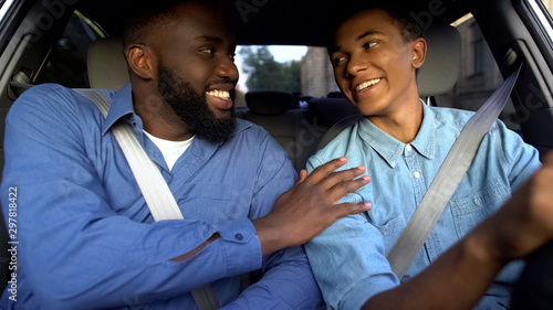 Smiling american father praising son learning to drive auto, parent help, family photo