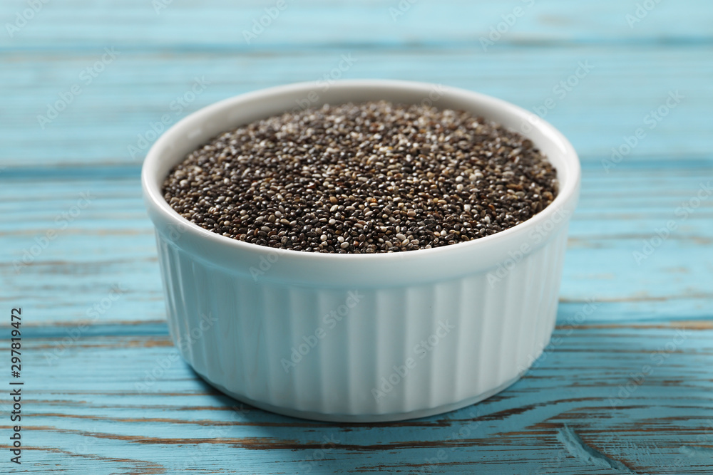 Chia in a white ceramic bowl on a blue wooden background. Chia in a white ceramic bowl on a blue wooden background.
