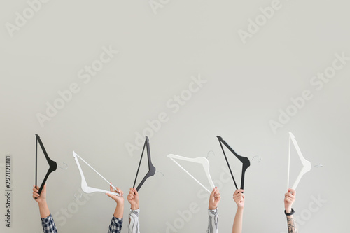 Female hands with clothes hangers on light background