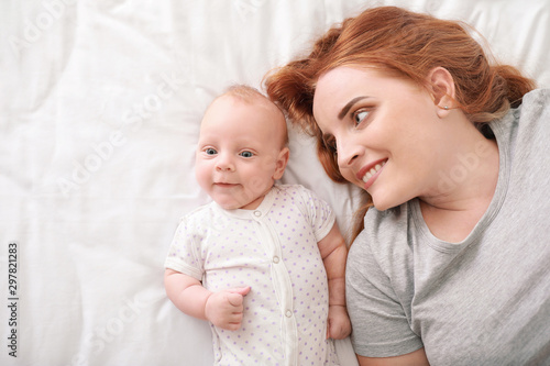 Mother with cute baby lying on bed, top view