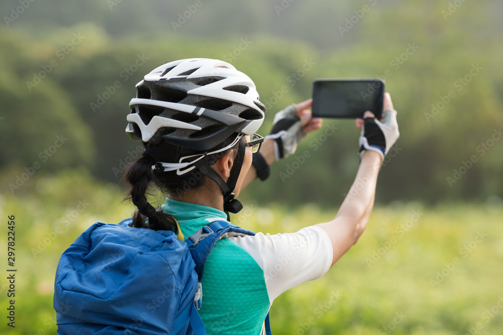Woman using smartphone taking photo while riding bike on sunny day in park Woman using smartphone taking photo while riding bike on sunny day in park